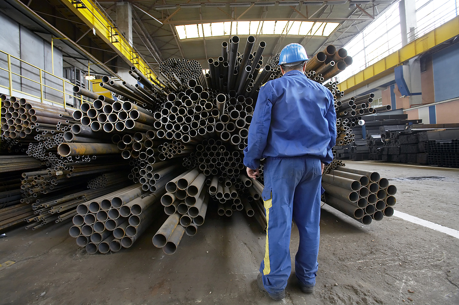 The image showcases a worker inspecting stacks of steel pipes in a warehouse setting, emphasizing the importance of quality and proper handling for large-scale construction projects.