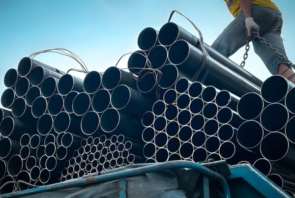 A group of steel pipes neatly arranged on a construction site, showcasing their polished metallic finish. The background features construction vehicles and materials, emphasizing the industrial and construction context. The image highlights the versatility and strength of steel pipe in large-scale projects.